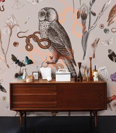 an owl sitting on top of a wooden dresser in front of a wall with flowers