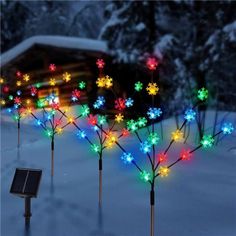 christmas lights are lit up in the snow near a fence and tree with snowflakes on it