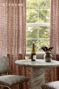 a table with two chairs and a bottle of wine on it in front of a window