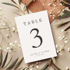 the table numbers are displayed on top of some white flowers and brown paper with green leaves