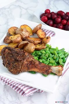 a white plate topped with meat, potatoes and green beans next to cranberries