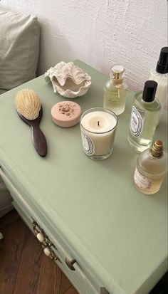 a green table topped with lots of bottles next to a candle and a wooden brush