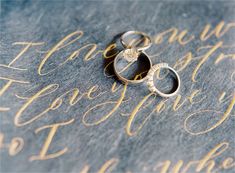 two wedding rings sitting on top of a piece of paper that says happily written in cursive writing