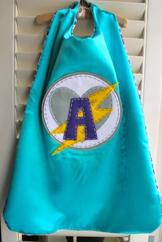 a blue cape hanging on the wall with a lightning bolt and letter a embroidered on it