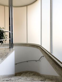 a curved staircase with white walls and marble flooring