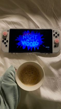 a cup of coffee sitting next to a nintendo wii game controller on top of a bed