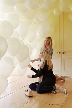 two women sitting on the floor in front of white balloons that look like they are floating