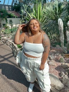 a woman standing in front of a cactus and palm tree with her hands on her head