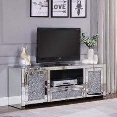 a silver tv stand with two framed pictures on the wall and a vase in front of it