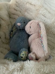 two stuffed animals sitting next to each other on a white fluffy bed sheet covered in blankets