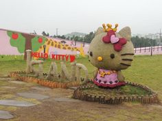 a hello kitty statue in the middle of a field next to a sign that says hello kitty