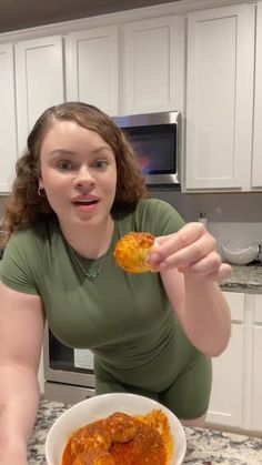 a woman sitting at a kitchen table eating food from a white bowl in front of her