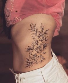 a woman's lower back tattoo with roses and leaves on her side ribcage