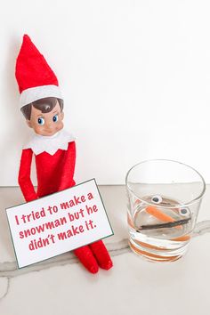 an elf holding a sign next to a glass of water