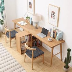 a wooden desk with two chairs and a laptop on it in front of a white wall