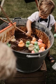 a little boy is playing with some rubber ducks in a big metal tub on the grass