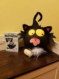 a black cat mask sitting on top of a wooden table next to a book and an egg