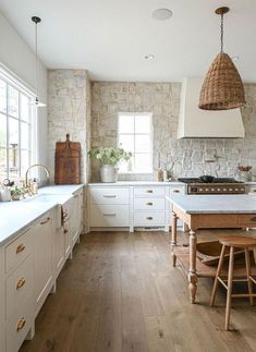 a large kitchen with white cabinets and wood flooring is pictured in this image, there are two pendant lights hanging from the ceiling