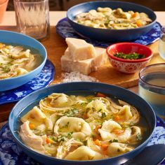 two blue bowls filled with pasta and vegetables on top of a table next to bread