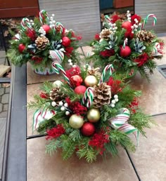 two christmas centerpieces sitting on top of a table covered in greenery and candy canes