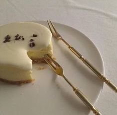 a white plate topped with a slice of cheesecake next to a knife and fork