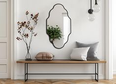 a mirror and some pillows on a wooden table in front of a white wall with a potted plant