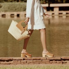 a woman in white dress walking by water with a basket on her hand and foot