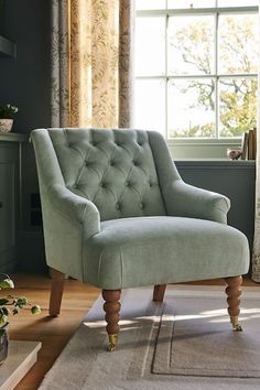 a green chair sitting on top of a rug in front of a window with curtains