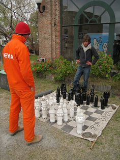 two men playing chess on a giant checker board in front of a brick building