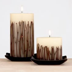 two candles sitting on top of each other with brown sticks in the candle holders behind them