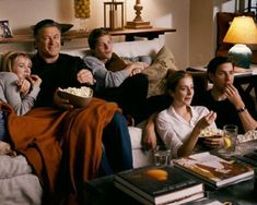 a group of people sitting on top of a couch eating popcorn and watching tv together