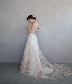 the back of a woman's wedding dress with flowers on it, standing against a wall