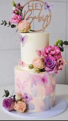 a three tiered cake with pink flowers and butterflies on the top is adorned with a wooden sign that says hey baby