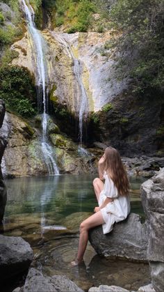 a woman sitting on top of a rock next to a waterfall