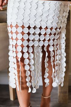 a close up of a woman's legs wearing sandals and a white skirt with circles on it