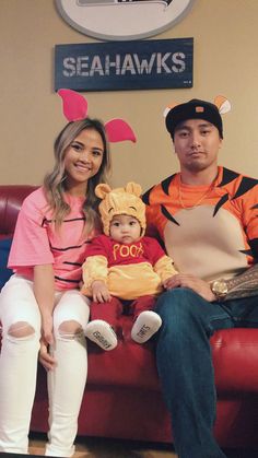 a man and woman sitting on a couch with a baby in winnie the pooh costume