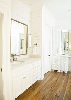 a white bathroom with wood floors and large mirrors on the wall above the sink, along with two sinks