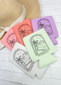 four different colored paper tags on top of a white sheet with a straw hat next to them