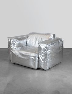 a shiny silver chair sitting on top of a cement floor next to a white wall