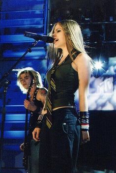 a woman standing in front of a microphone on top of a stage with another person behind her