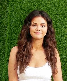 a young woman standing in front of a green grass wall with her hands on her hips