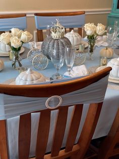 the table is set with white roses and silver pumpkins on it, along with other decorations