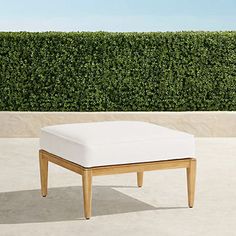 a white foot stool sitting on top of a cement floor next to a green hedge