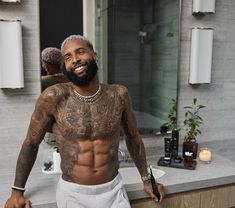 a man with tattoos standing in front of a bathroom sink and looking at the camera