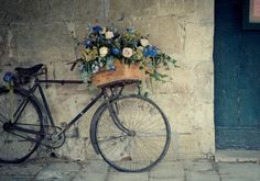 an old bicycle with flowers in the basket on it's front wheel, leaning against a stone wall