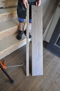 a man standing next to some wood planks on top of a wooden floor in front of stairs