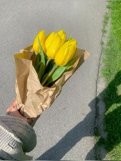 a person holding a bouquet of yellow tulips in their hand on the sidewalk