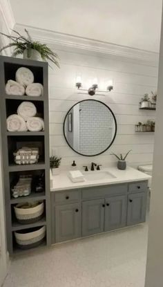 a bathroom with gray cabinets and white towels on the shelves, along with a round mirror