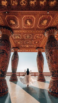 a woman in a white dress is standing under an ornately decorated structure with columns