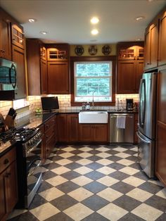 a kitchen with black and white checkered flooring, stainless steel appliances and wooden cabinets